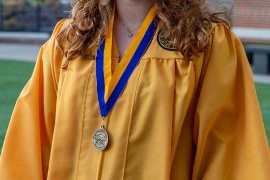 a graduate wearing a gold Honors EXCEL robe and lanyard medallion
