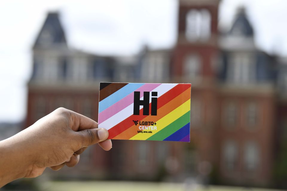 A hand holding up a promotional card for the LGBTQ+ Center that reads 'Hi.' in black text.